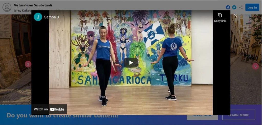 Kuvakaappaus tanssivideosta, jossa kaksi naista tanssivat samba-aiheisen taustan edessä.